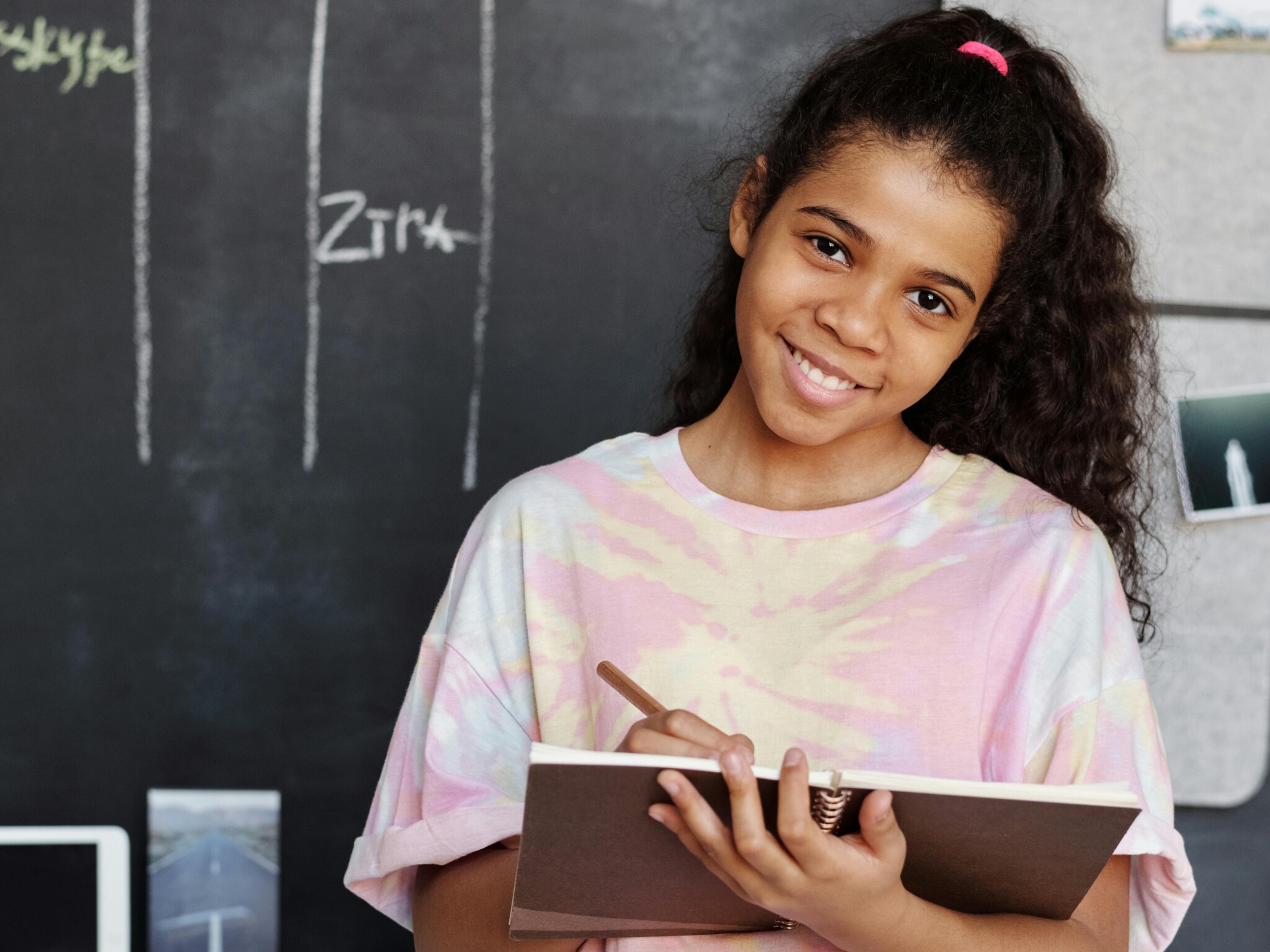 A girls holding a writing tablet in a classroom and smiling.